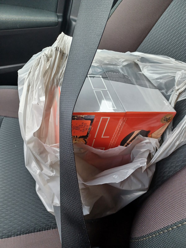 A Scott Pilgrim 20th Anniversary, Color Edition box set in a plastic bag on a car seat. The box set is secured to the seat using a seat belt.